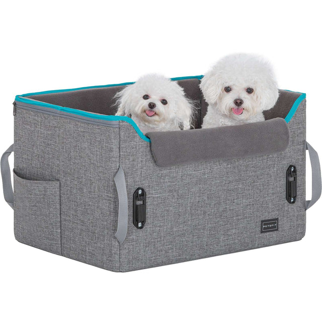 Two small white pups peek out from a gray dog car seat with teal edging, showing spacious interior and a cozy cushion.