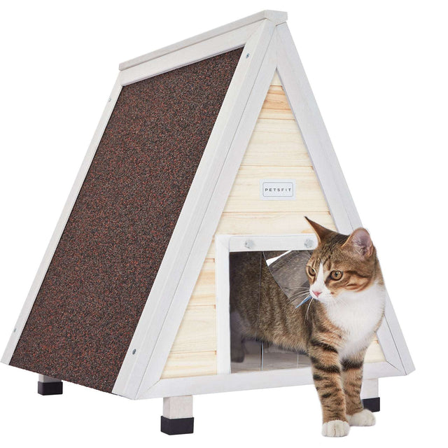 Light wood A-frame outdoor cat house with white trim and weatherproof roof, as a tabby cat stands at the clear flap doorway.
