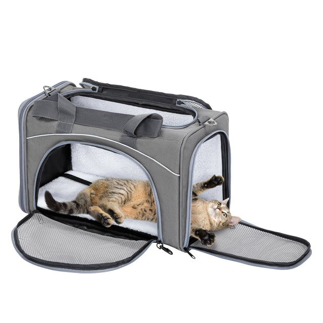 Tabby cat lounges inside open gray cat carrier with front and side mesh doors unzipped, stretching on plush interior pad.