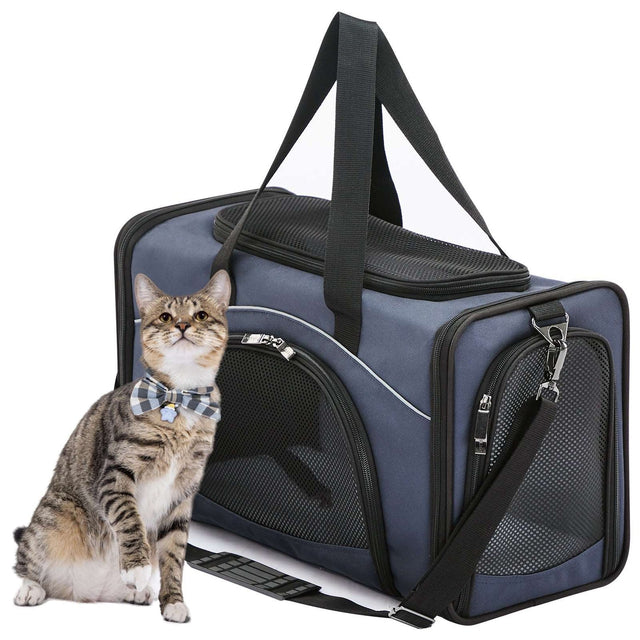 Tabby cat in a bow tie sits beside a navy pet carrier with mesh windows, top handle straps, and detachable shoulder strap.