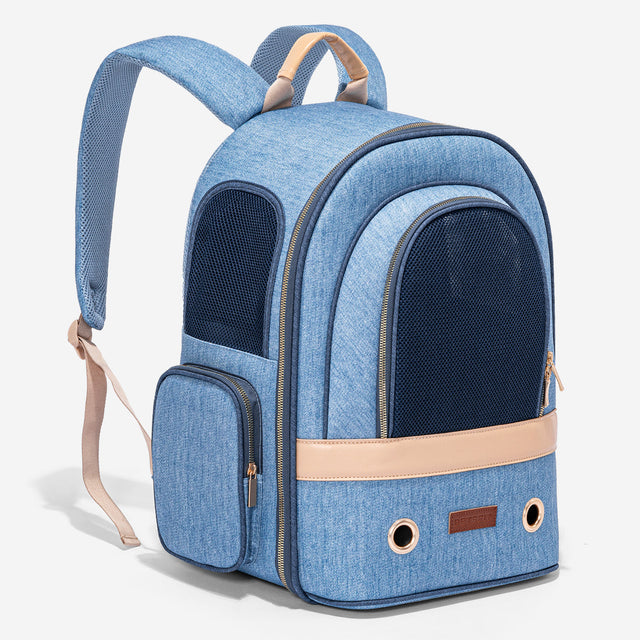 Light blue pet backpack with mesh side windows, front zip opening, and side pocket, styled with tan trim on a gray backdrop
