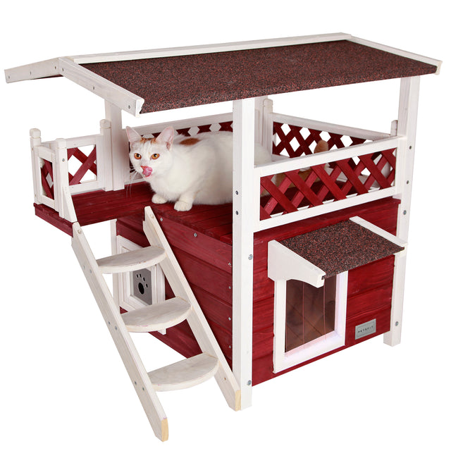 White and red wooden cat house with a covered upper deck, side ladder, and sheltered lower doorway while a cat lounges above.