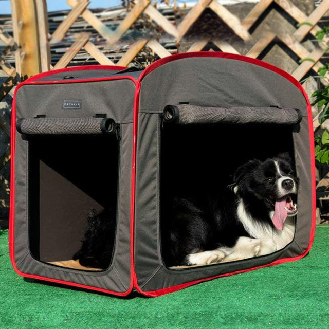 Brown and red collapsible dog crate set on grass outdoors, with a black-and-white dog resting inside the open side entry.