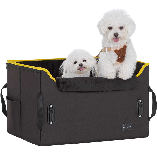 Two fluffy white dogs sit side by side in a roomy black dog booster seat with yellow trim and a soft front bolster.