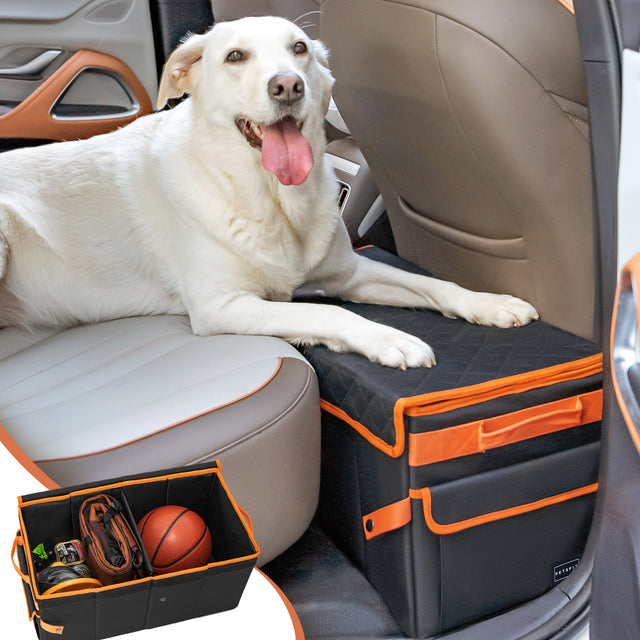 White Labrador dog lying on PETSFIT black and orange car seat extender in car backseat, with inset showing large storage compartment containing basketball and dog supplies, up to 90 lbs capacity