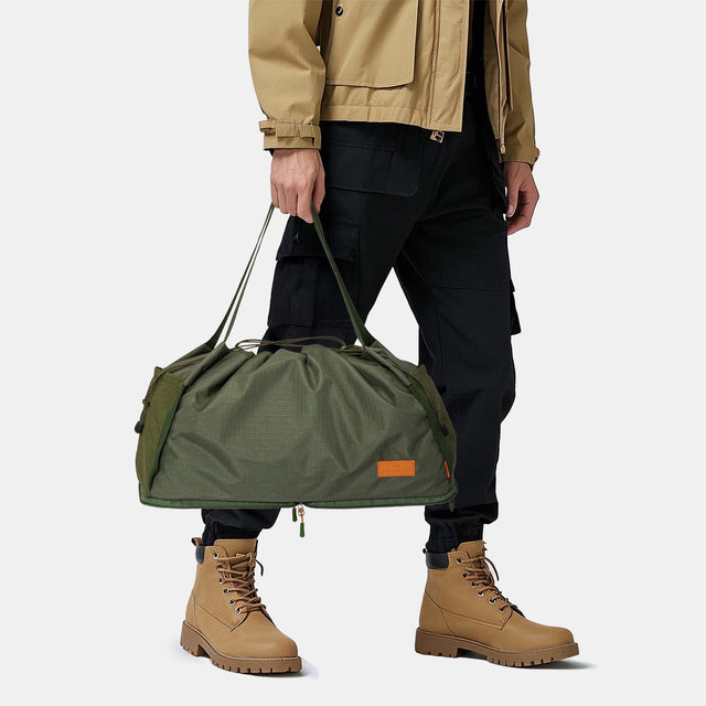 Olive dog backpack gear bag in side profile, showing a curved base zipper and pocket panels.