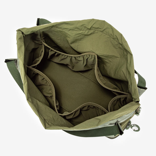 Olive gear bag for dog backpack trips, carried by hand with long handles, side pockets, and tan work boots.