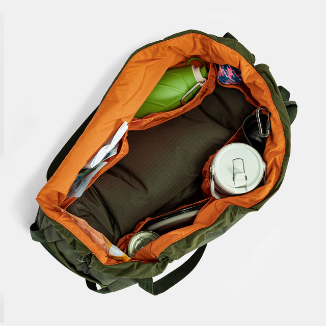 Olive gear bag for dog backpack trips, carried by hand with long handles, side pockets, and tan work boots.