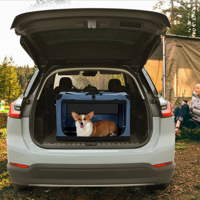 Blue travel dog crate secured in an SUV cargo area at a campsite, with a corgi resting inside for safe road trips.