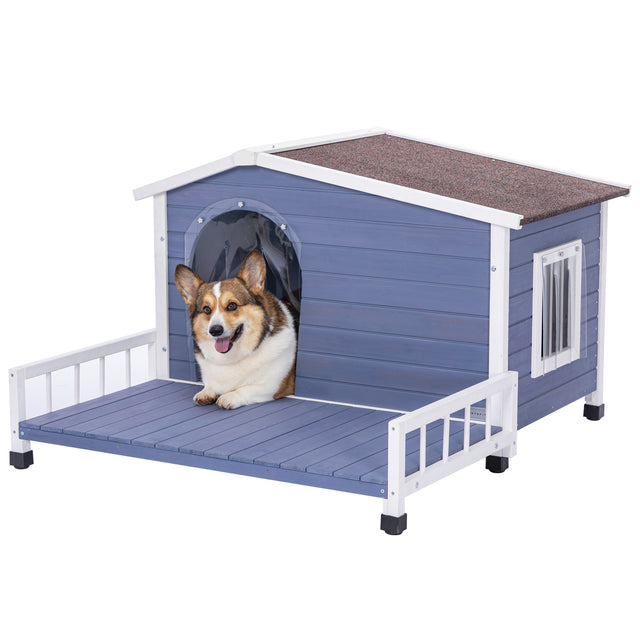 Corgi peeks out happily from a blue wooden dog house, lounging on the porch deck with side rails and a shingled roof.
