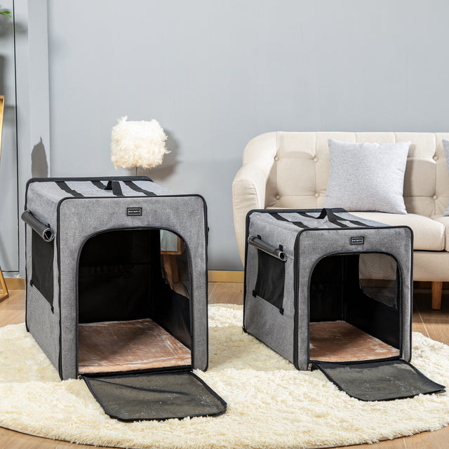 Two gray soft dog crate sizes are staged in a living room by a sofa, both with front doors open and plush mats inside.