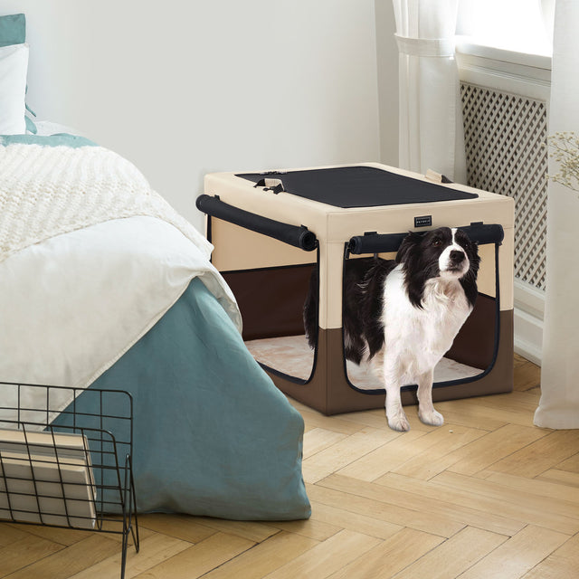 Border collie stands in a beige soft dog crate beside a bed and bright window, blending neatly into a cozy bedroom setting.