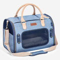 Light blue denim pet carrier with navy mesh windows, tan handles, and adjustable shoulder strap for breathable travel comfort.