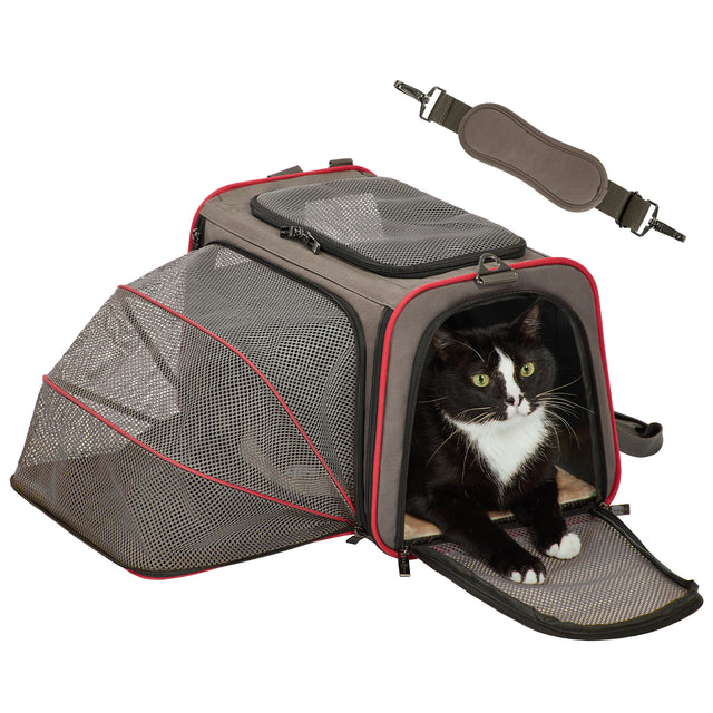 Tuxedo cat rests in a gray and red soft-sided cat carrier with expanded mesh extension and open front entry for stretching out.