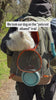 White terrier settles into an olive pet carrier backpack with water bowl and bottle packed, riding along a sunny wooded trail